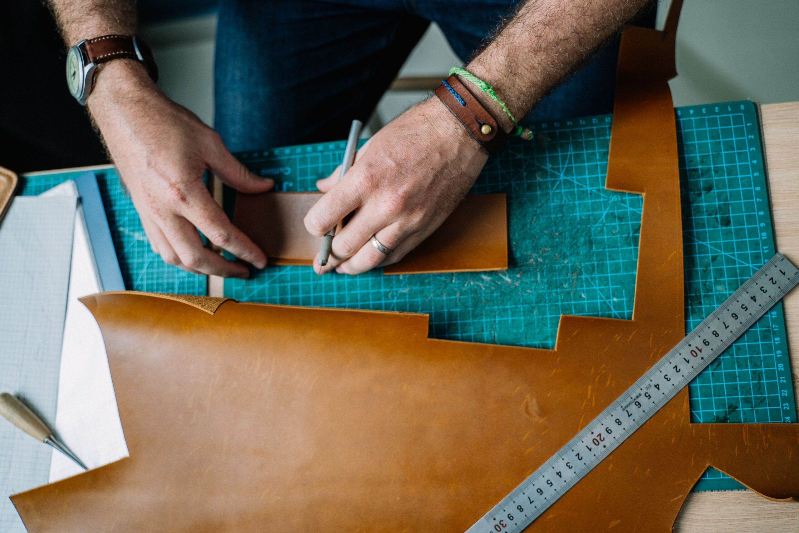 Close-up of hands crafting leather on a cutting board, showcasing artisan skills.